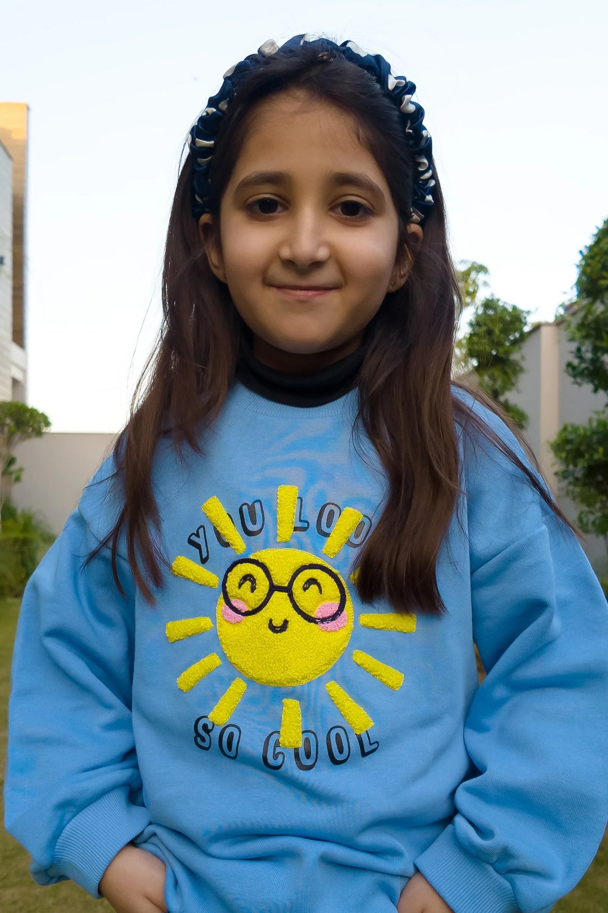 Smiling girl in blue kids sweatshirt with cute sun print and headband outdoors