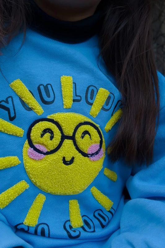 Child wearing blue sweatshirt with embroidered sun and 'You look so good' text